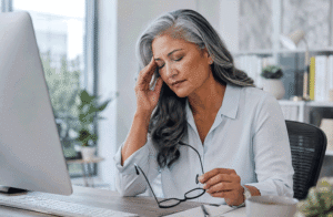 Aiello Eye Institute image for improve your vision naturally showing a 60-year-old woman experiencing digital eye strain while working at a computer in a modern office.